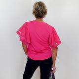 Person wearing a bright pink blouse with sheer sleeves against a white wall.