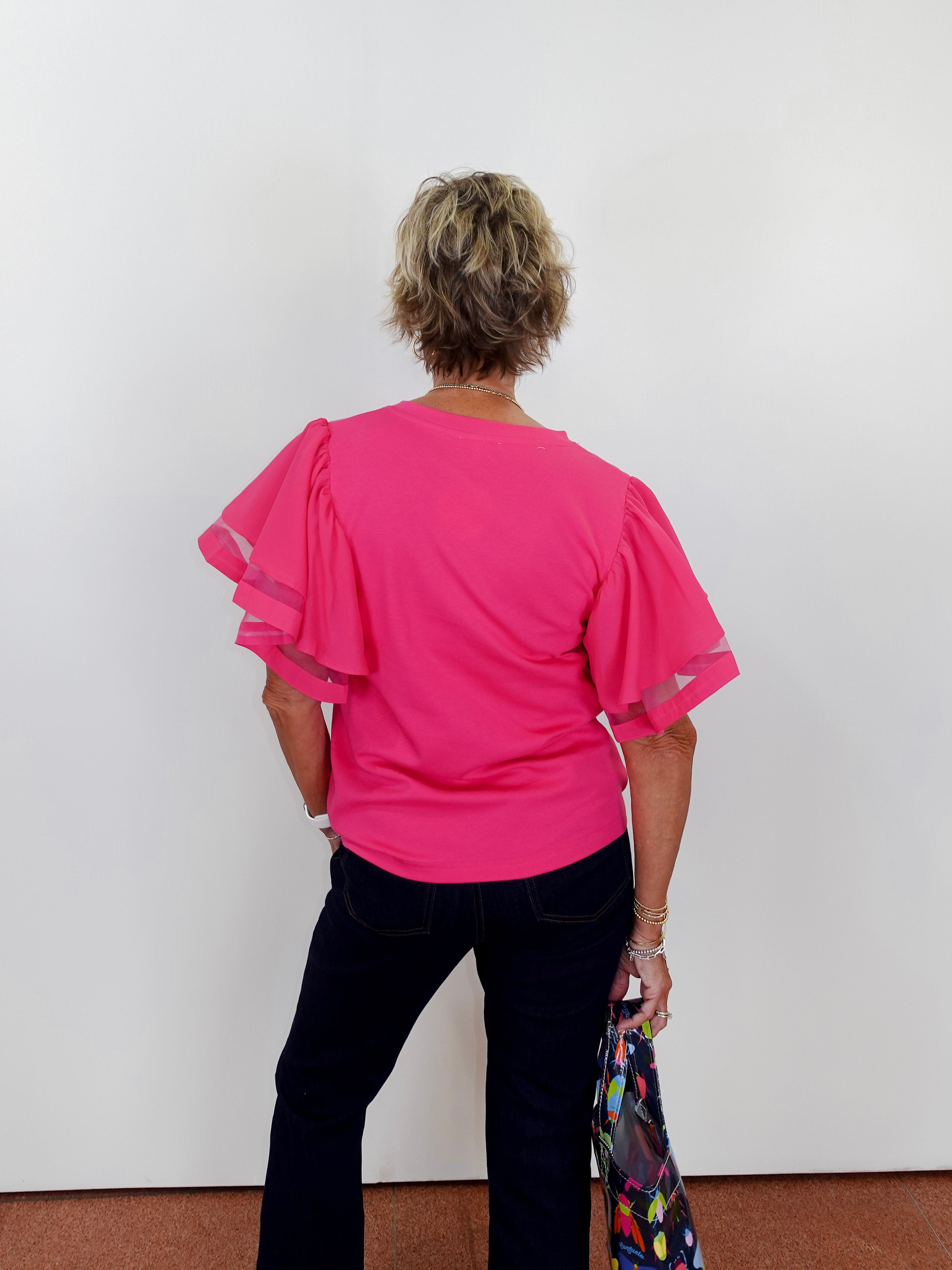 Person wearing a bright pink blouse with sheer sleeves against a white wall.