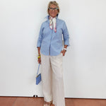 Person wearing a blue shirt and white pants against a white wall.