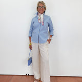 Person wearing a blue shirt and white pants against a white wall.