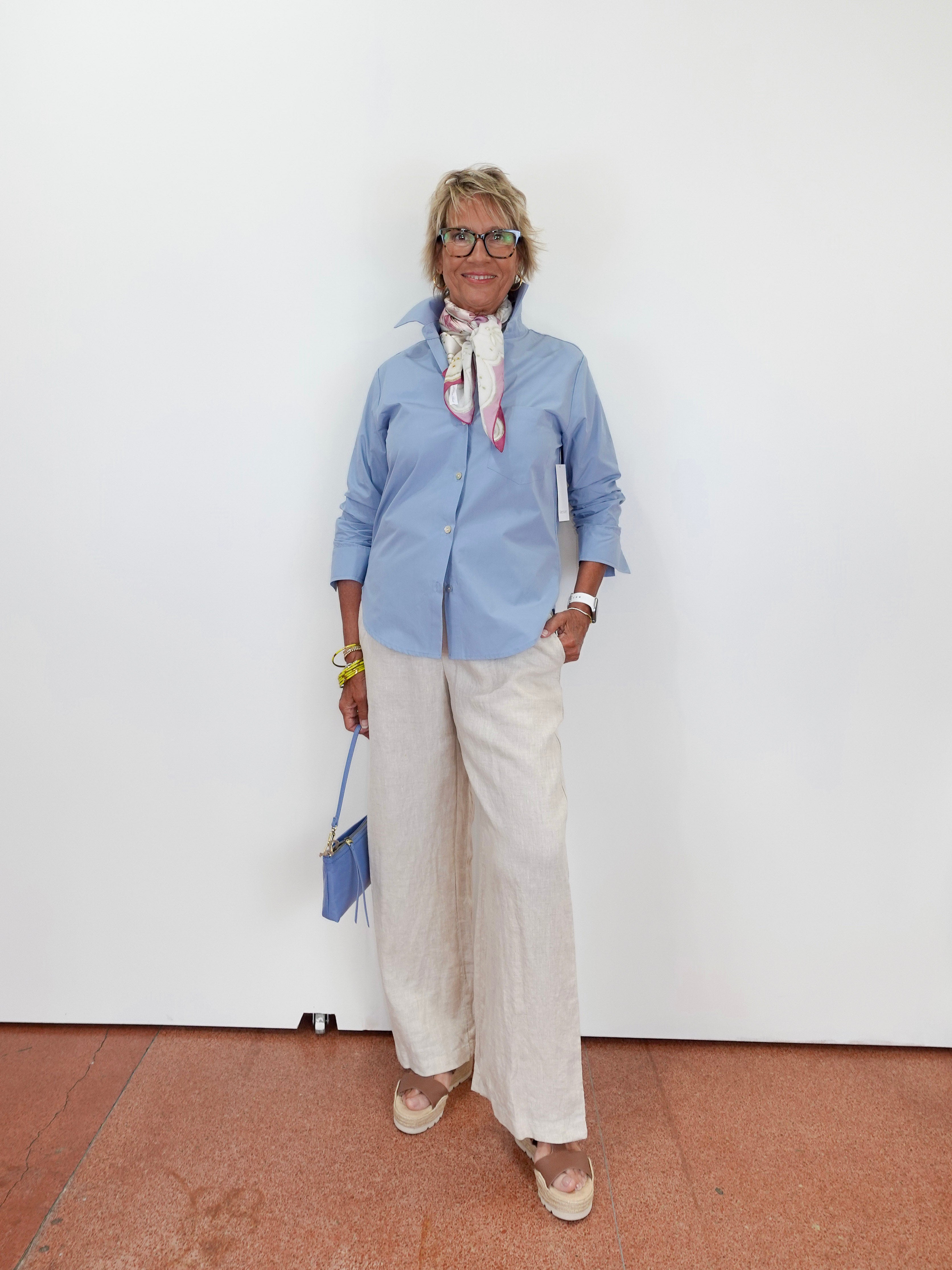 Person wearing a blue shirt and white pants against a white wall.