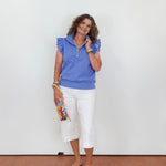 Woman wearing a blue top and white pants against a plain background