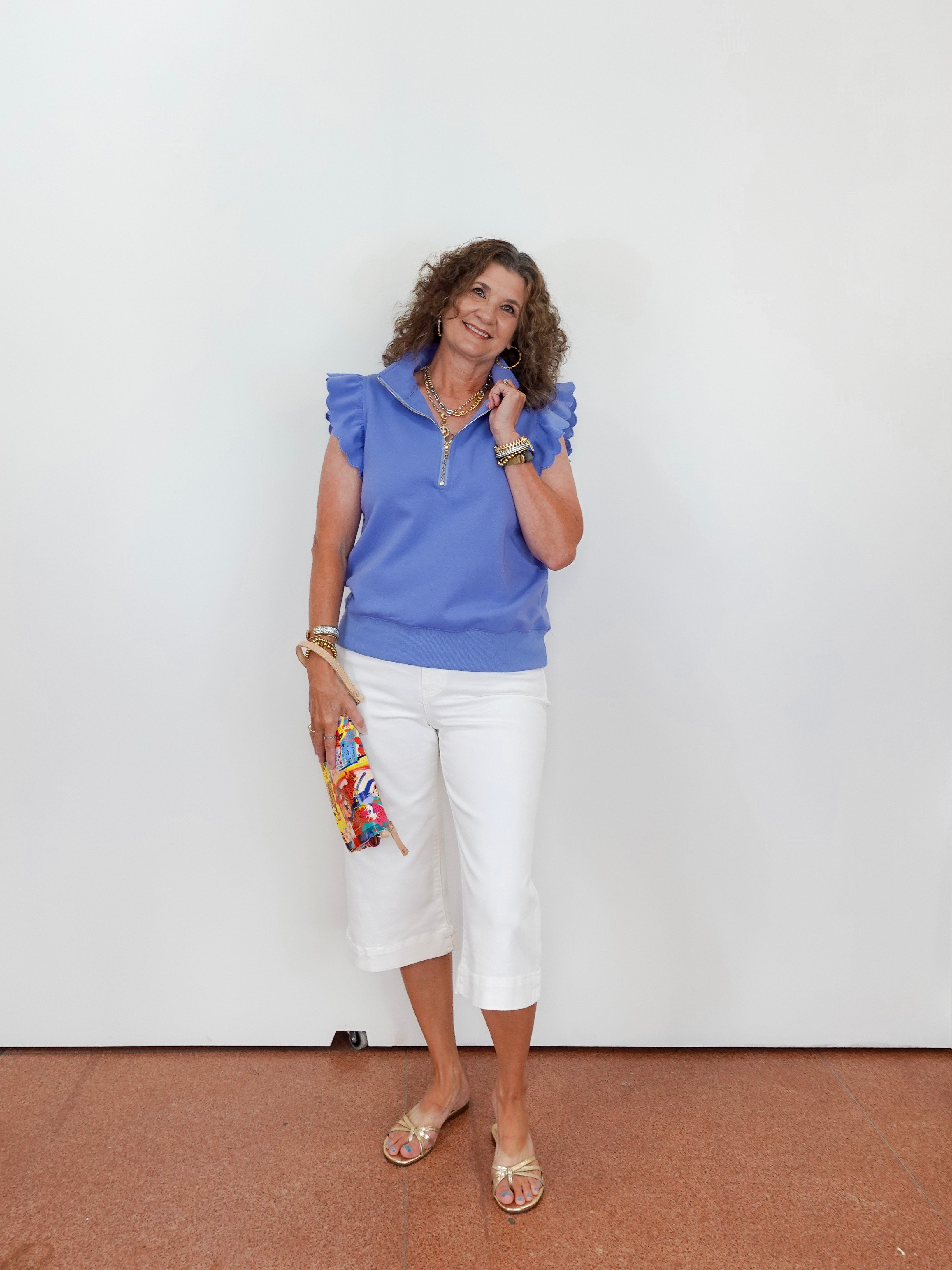 Woman wearing a blue top and white pants against a plain background