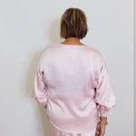 woman wearing a pink Karen Kane satin top against a white background. 