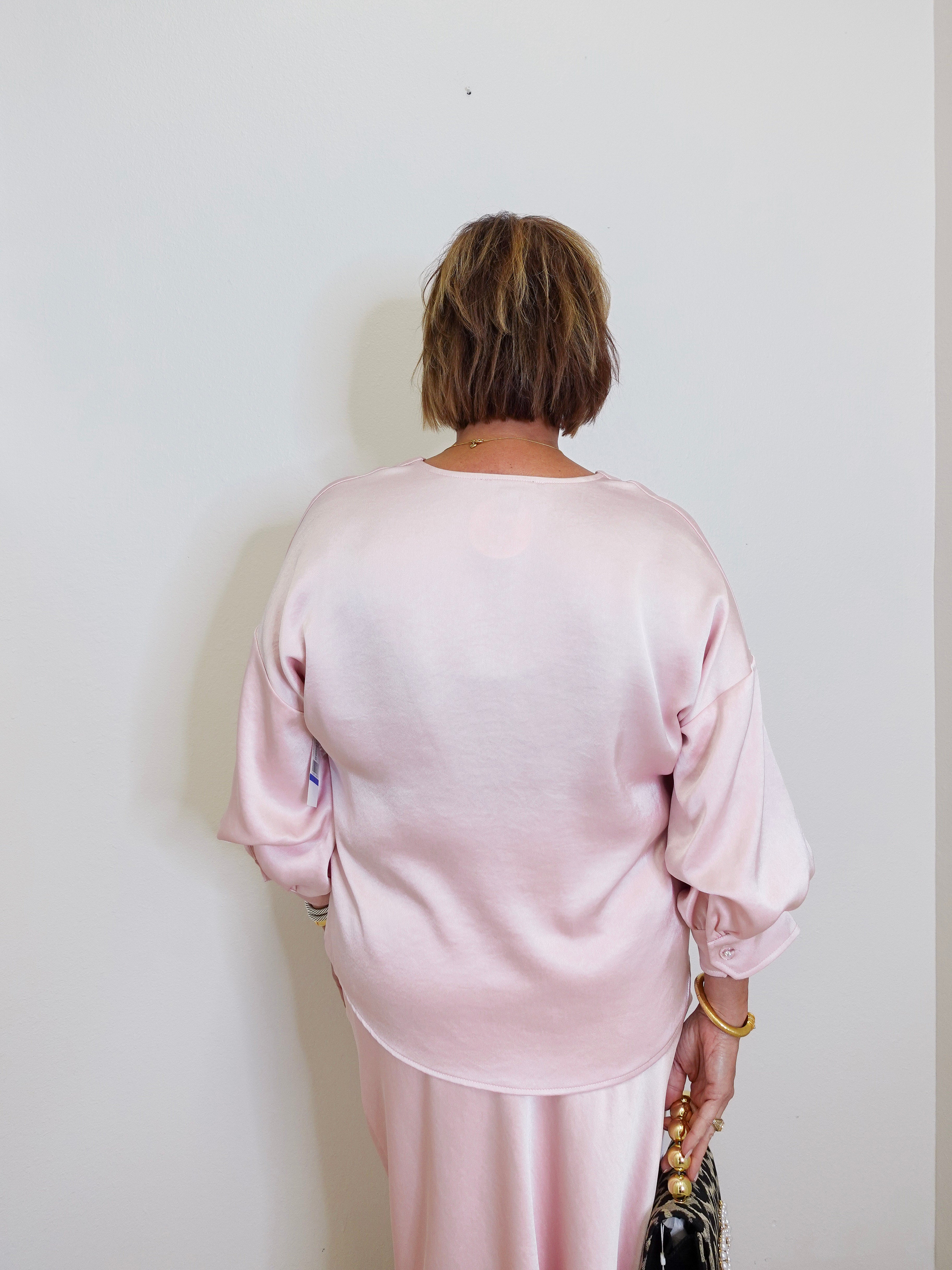 woman wearing a pink Karen Kane satin top against a white background. 