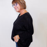 Woman wearing a black sweater and blue jeans against a white background