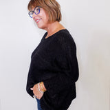 Woman wearing a black sweater and blue jeans against a white background