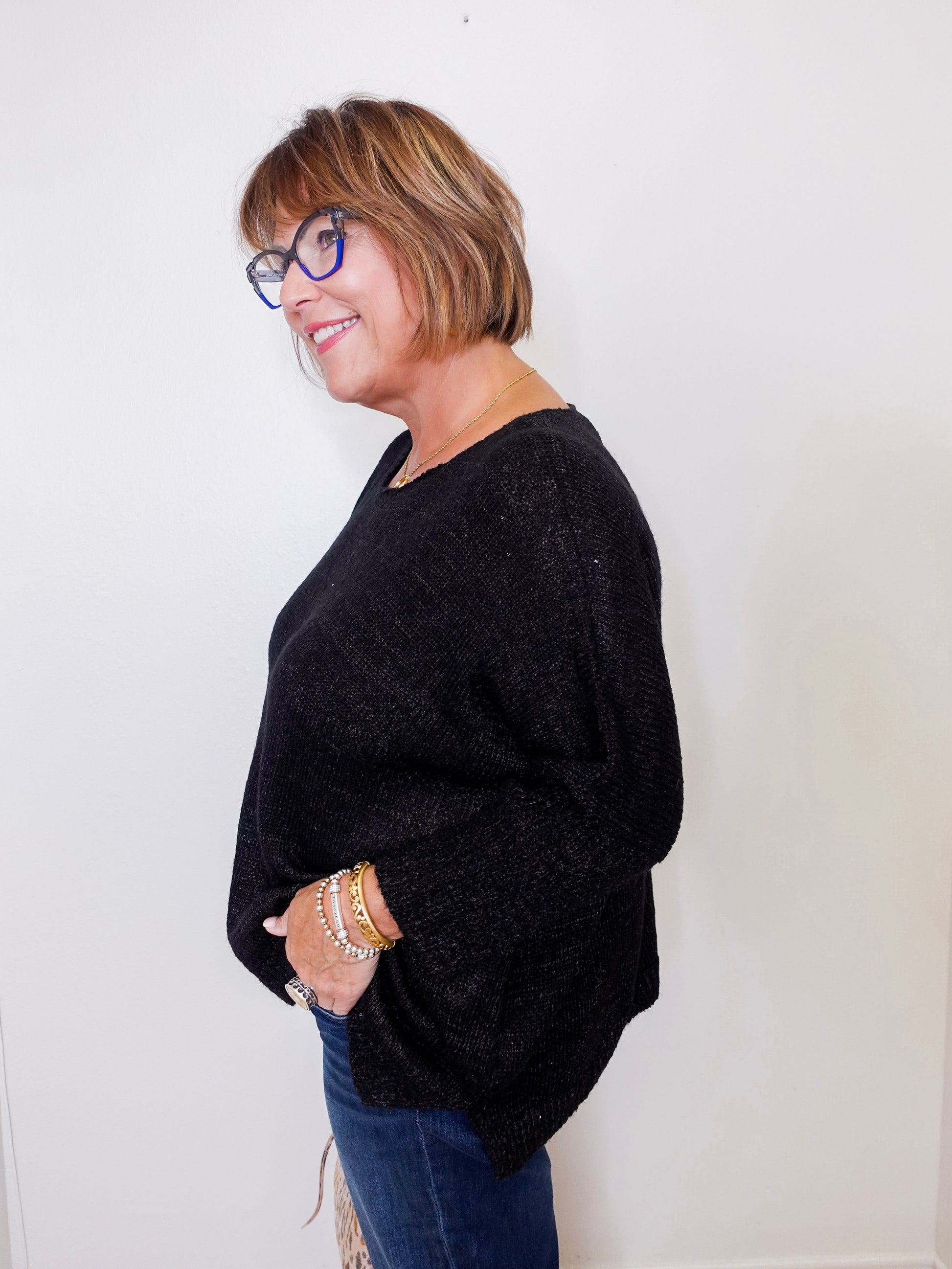 Woman wearing a black sweater and blue jeans against a white background