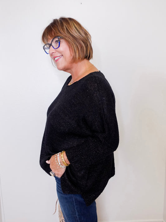 Woman wearing a black sweater and blue jeans against a white background