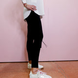Person wearing black pants and white sneakers against a pink wall.