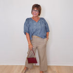 Woman wearing a blue blouse and beige pants with a red handbag against a white wall.