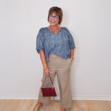 Woman wearing a blue blouse and beige pants with a red handbag against a white wall.