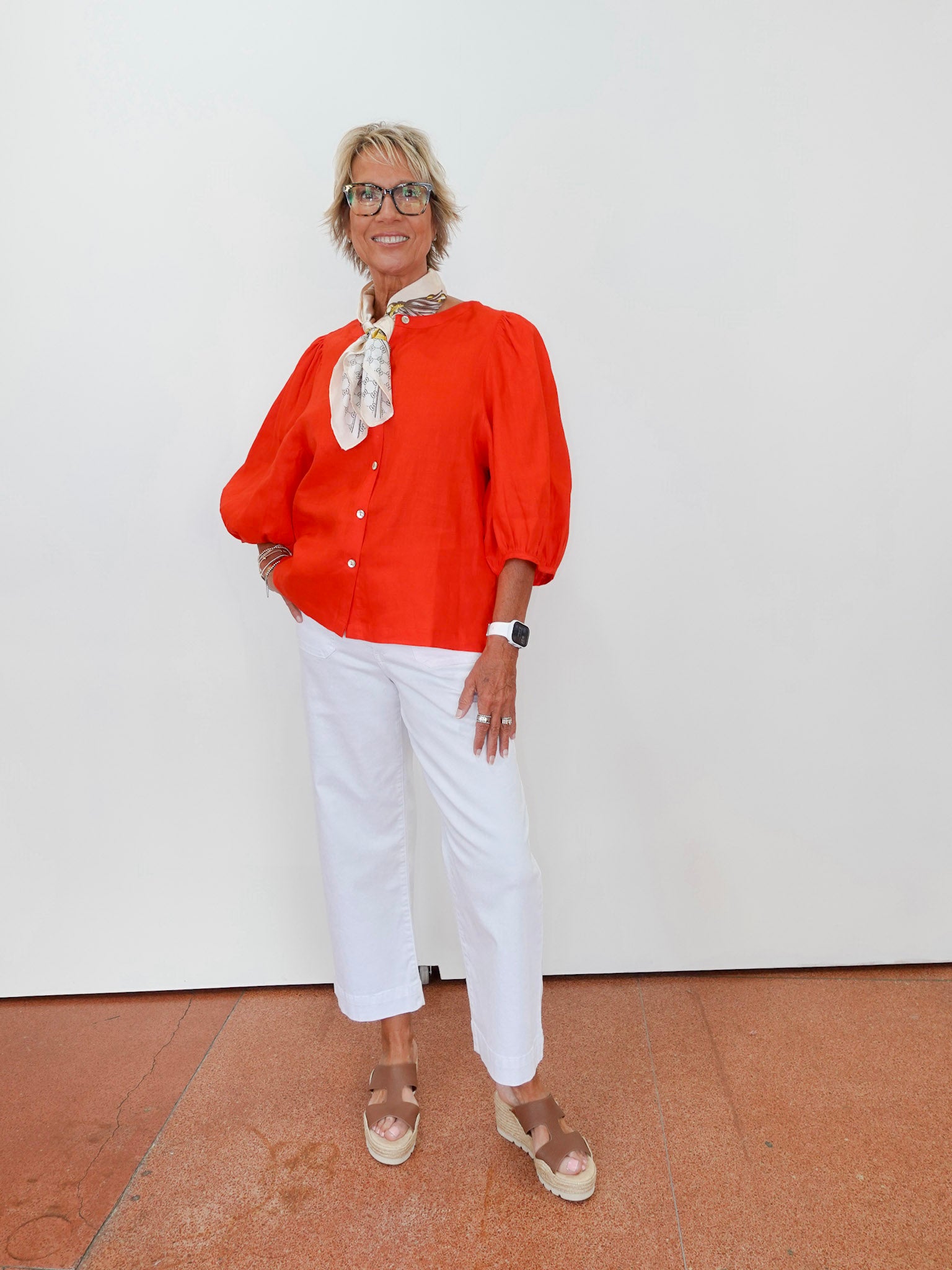 Woman wearing an orange blouse, white pants, and brown shoes on a plain background