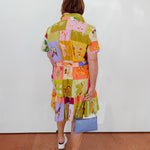 Person wearing a colorful patchwork dress with a white wall background