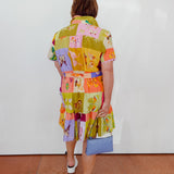 Person wearing a colorful patchwork dress with a white wall background