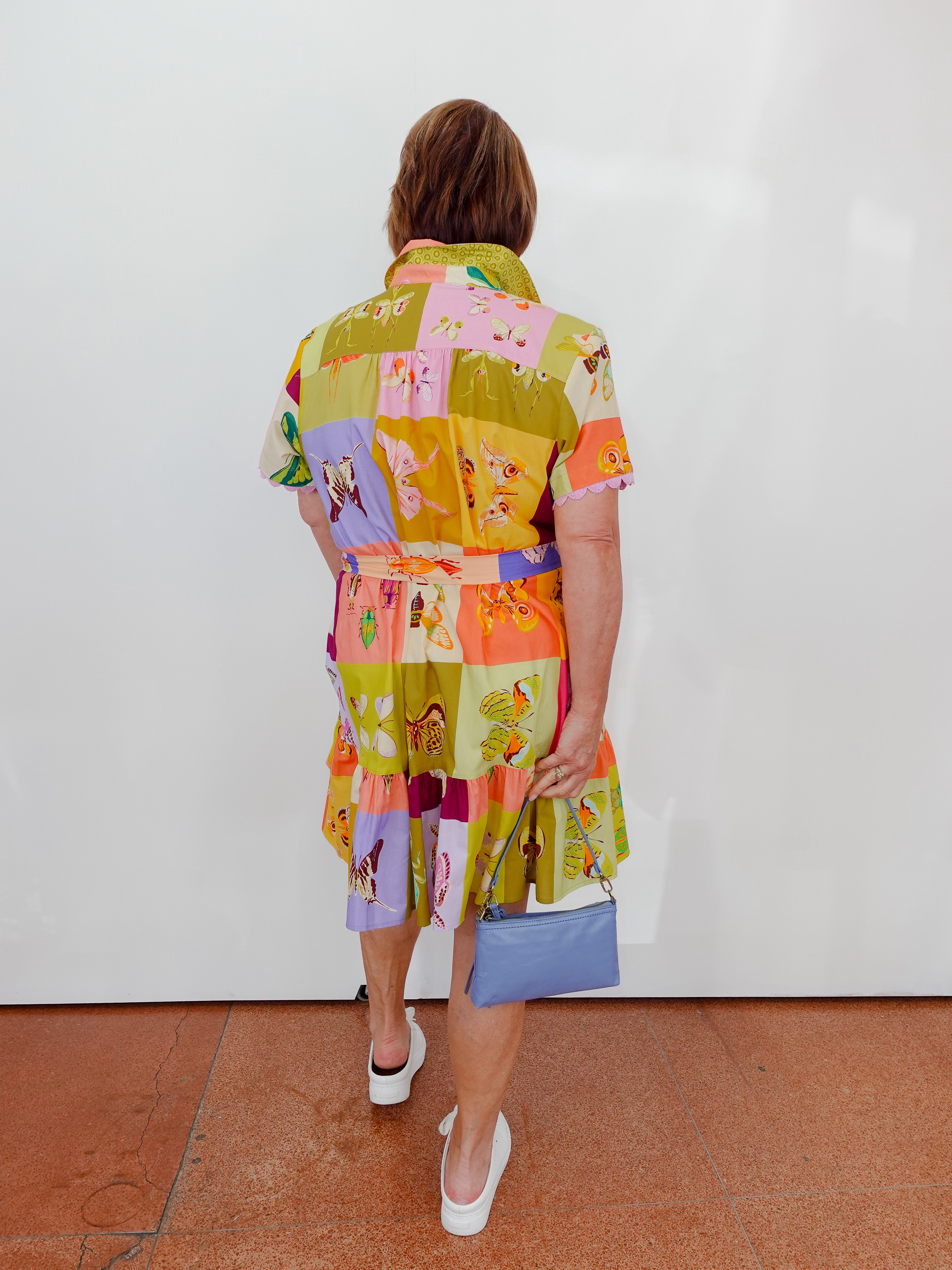Person wearing a colorful patchwork dress with a white wall background