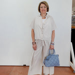 Woman in light-colored outfit holding a blue handbag against a white wall.