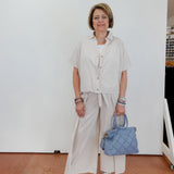 Woman in light-colored outfit holding a blue handbag against a white wall.
