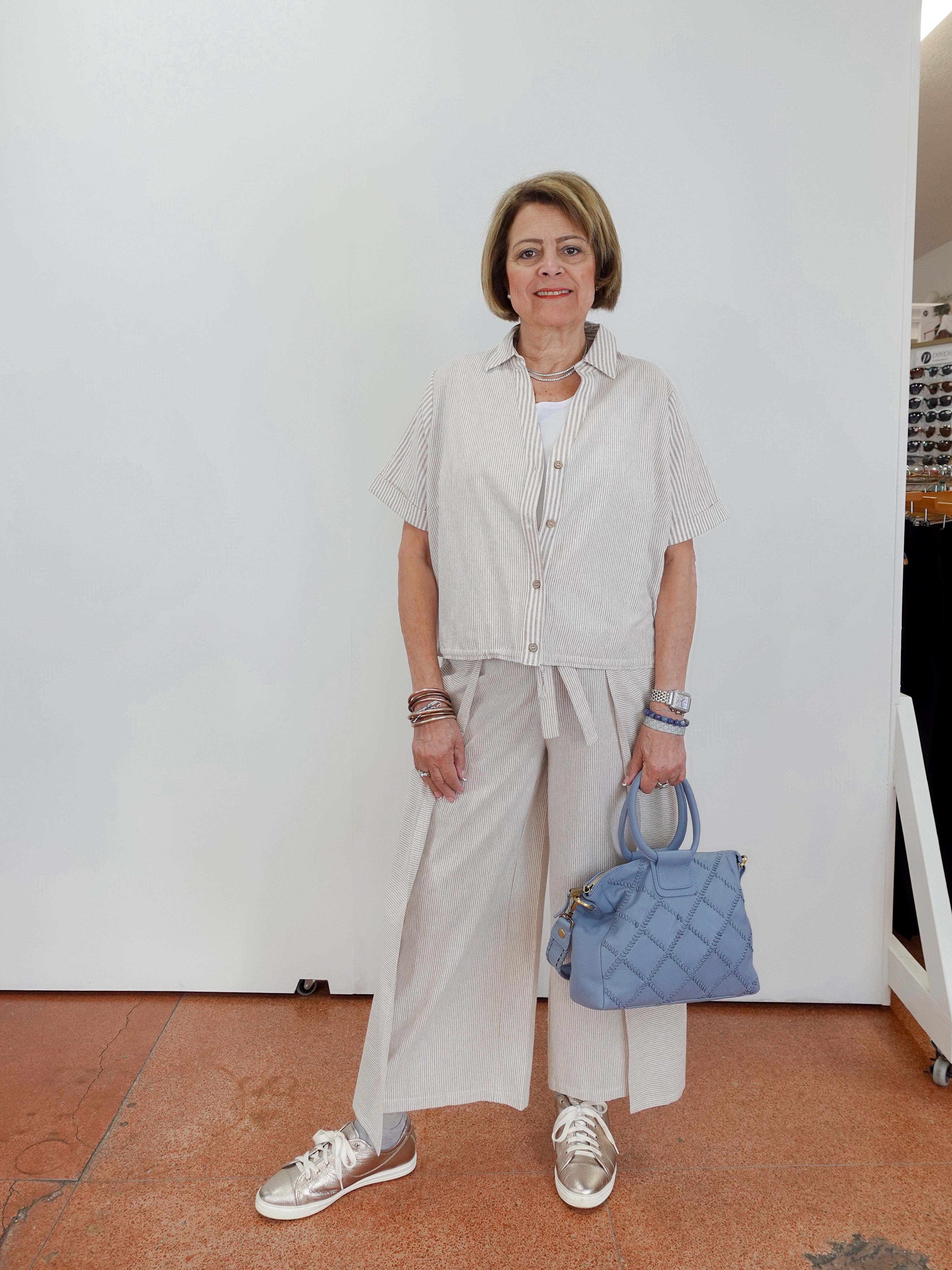 Woman in light-colored outfit holding a blue handbag against a white wall.