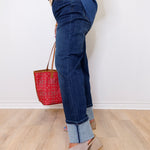 Person wearing blue jeans and holding a red handbag on a light wooden floor.