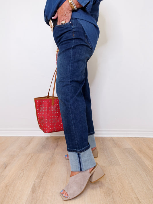 Person wearing blue jeans and holding a red handbag on a light wooden floor.