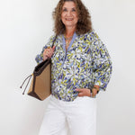 Woman wearing a floral blouse and white shorts, holding a handbag against a white background