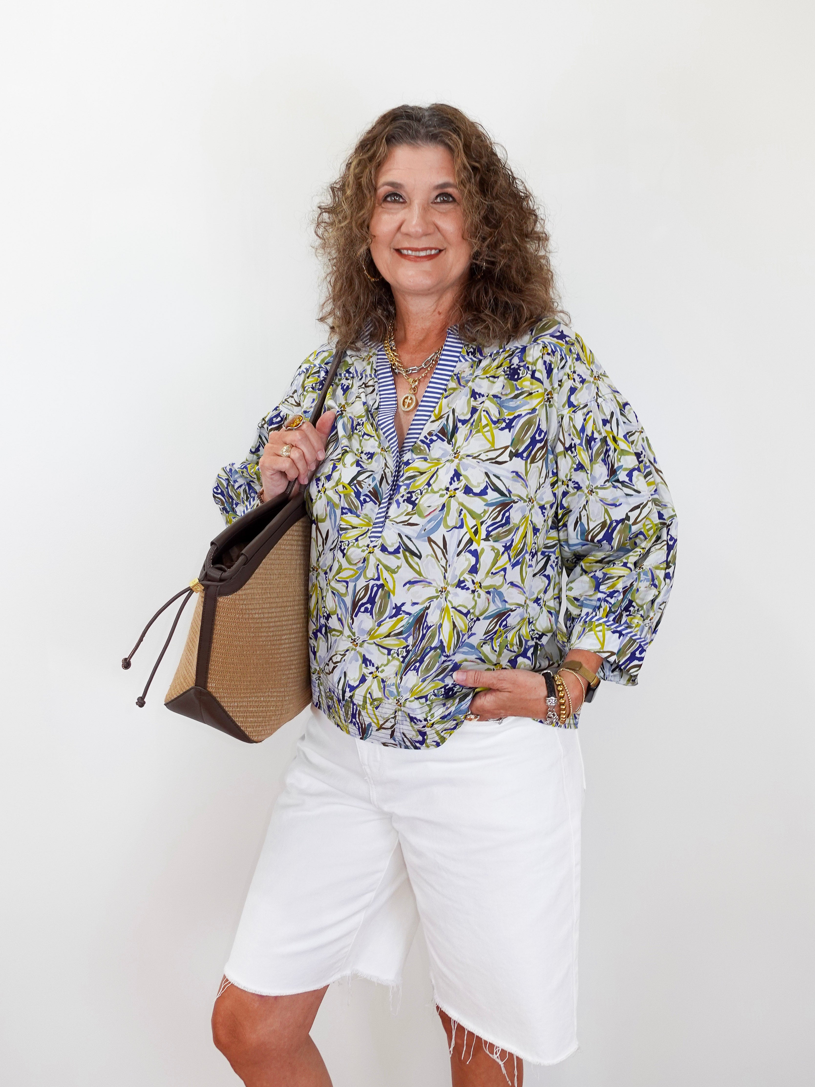 Woman wearing a floral blouse and white shorts, holding a handbag against a white background