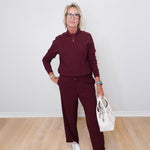 Woman in burgundy outfit holding a white handbag against a plain background