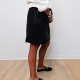 Person wearing a black skirt and white sweater against a white wall.