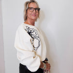 Woman wearing a white sweater with black abstract design against a plain background
