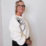 Woman wearing a white sweater with black abstract design against a plain background