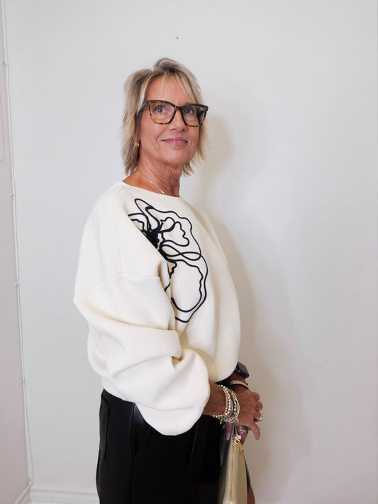 Woman wearing a white sweater with black abstract design against a plain background
