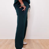 Person wearing dark green jogger pants and white sneakers on a light wooden floor.