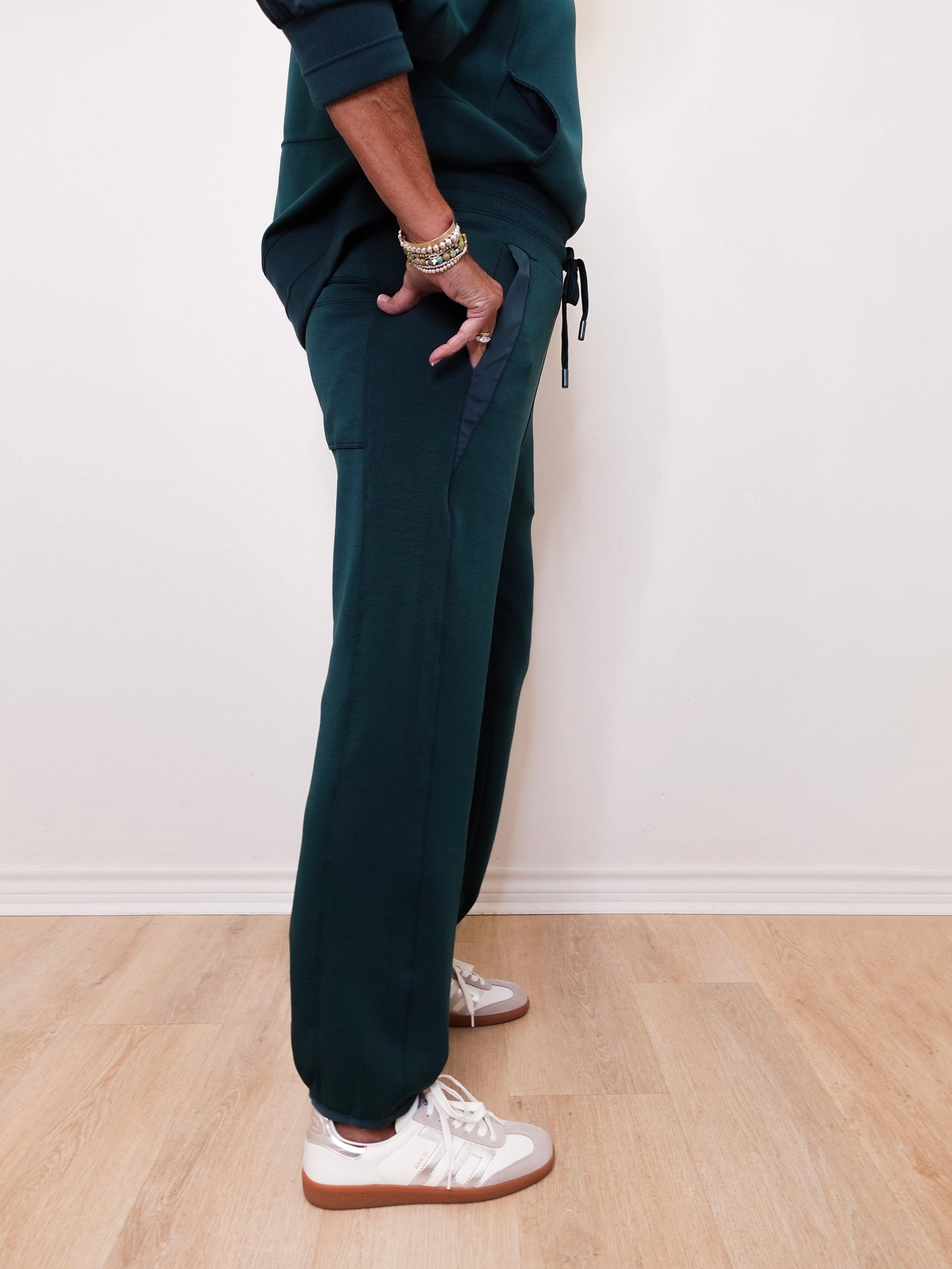 Person wearing dark green jogger pants and white sneakers on a light wooden floor.
