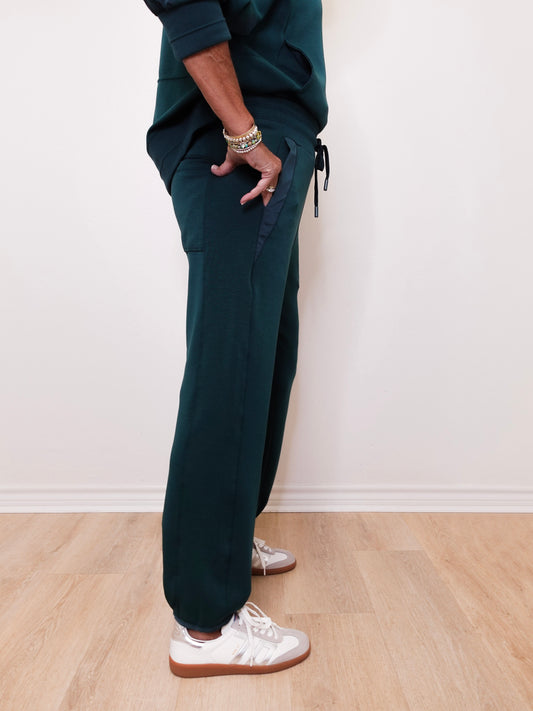 Person wearing dark green jogger pants and white sneakers on a light wooden floor.
