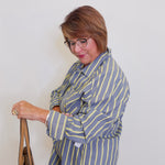Woman wearing a blue and yellow striped blazer holding a brown bag against a white background
