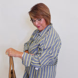 Woman wearing a blue and yellow striped blazer holding a brown bag against a white background
