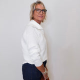 Woman wearing a white sweater and dark pants against a plain background
