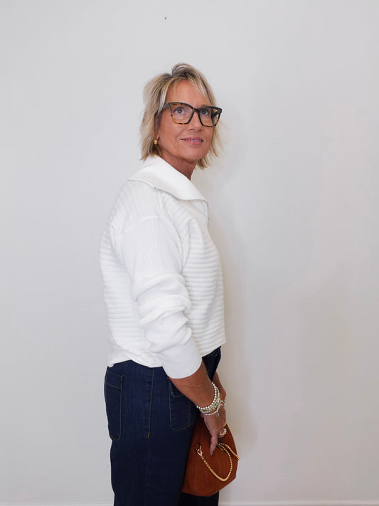 Woman wearing a white sweater and dark pants against a plain background