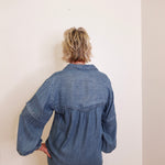 Person wearing a blue denim shirt against a white wall