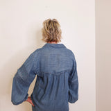 Person wearing a blue denim shirt against a white wall