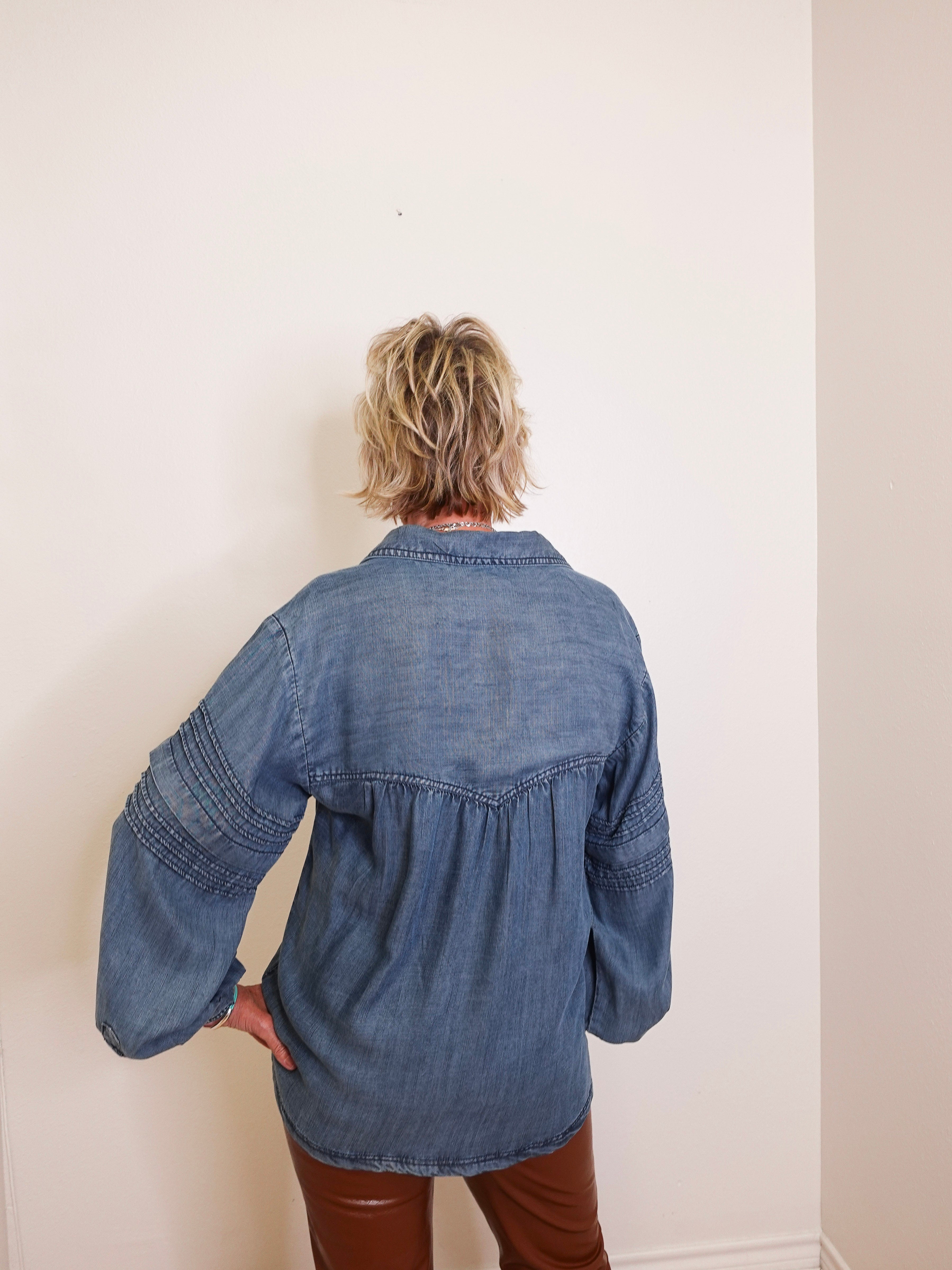 Person wearing a blue denim shirt against a white wall