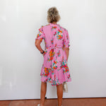 Woman wearing a pink floral dress against a white wall.