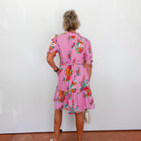 Woman wearing a pink floral dress against a white wall.
