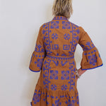 Woman wearing a brown dress with blue patterns against a white wall