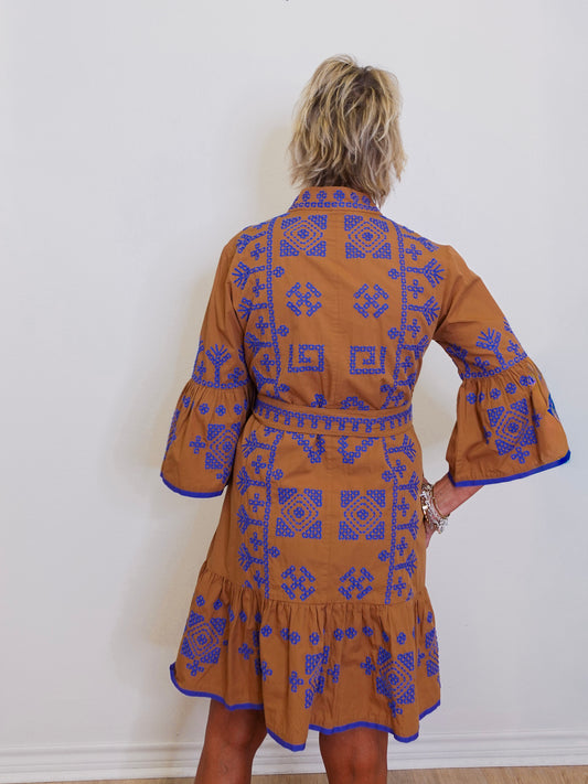 Woman wearing a brown dress with blue patterns against a white wall