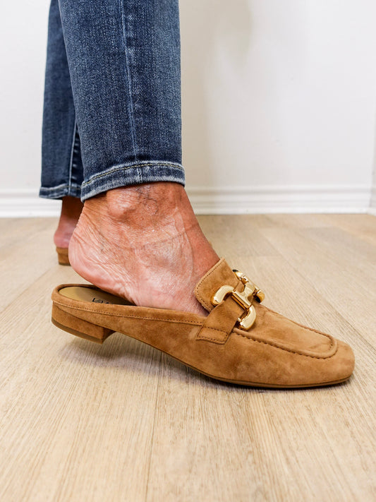 Brown suede loafer worn with blue jeans on a wooden floor.