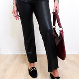 Person wearing black pants and black loafers with a maroon handbag on a light wooden floor.