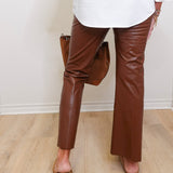 Person wearing brown leather pants and a white top, standing on a wooden floor.