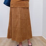 Person wearing a brown suede skirt and navy shoes on a light wooden floor.